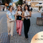 Trzy wolontariuszki festiwalu filmowego idą wieczorem brukowaną ulicą w centrum Radomia. Na szyjach mają identyfikatory, w dłoniach festiwalowe materiały. W prawym dolnym rogu znajduje się napis: „Filmowy wolontariat?”.