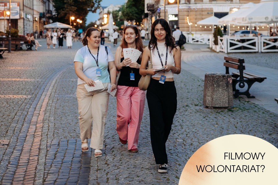Trzy wolontariuszki festiwalu filmowego idą wieczorem brukowaną ulicą w centrum Radomia. Na szyjach mają identyfikatory, w dłoniach festiwalowe materiały. W prawym dolnym rogu znajduje się napis: „Filmowy wolontariat?”.