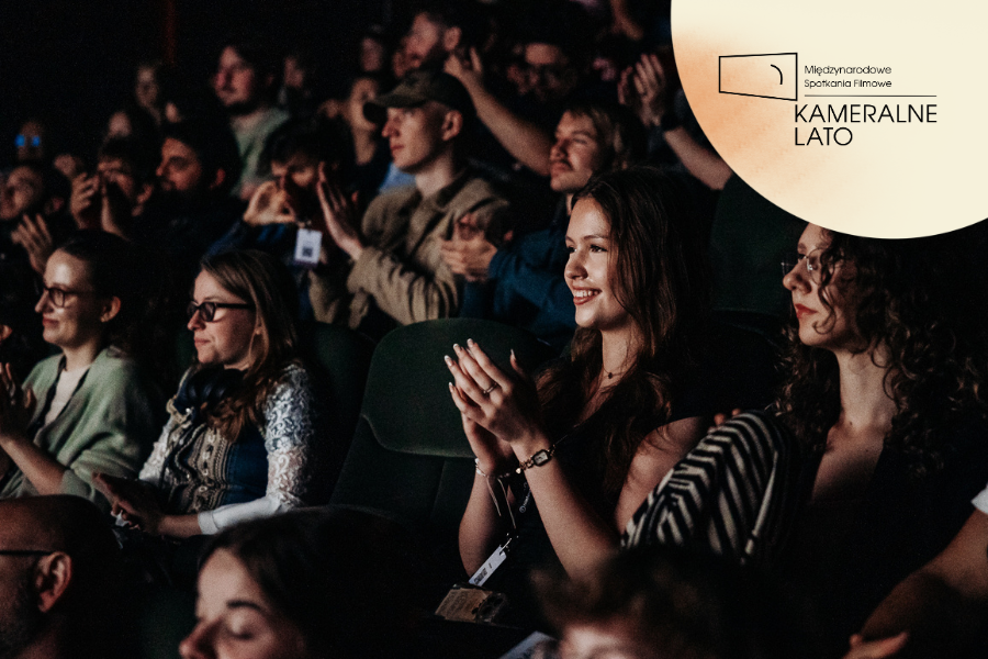 Publiczność w sali kinowej bije brawo podczas pokazu filmowego. Na pierwszym planie uśmiechnięta uczestniczka festiwalu, w prawym górnym rogu logo Kameralnego Lata.